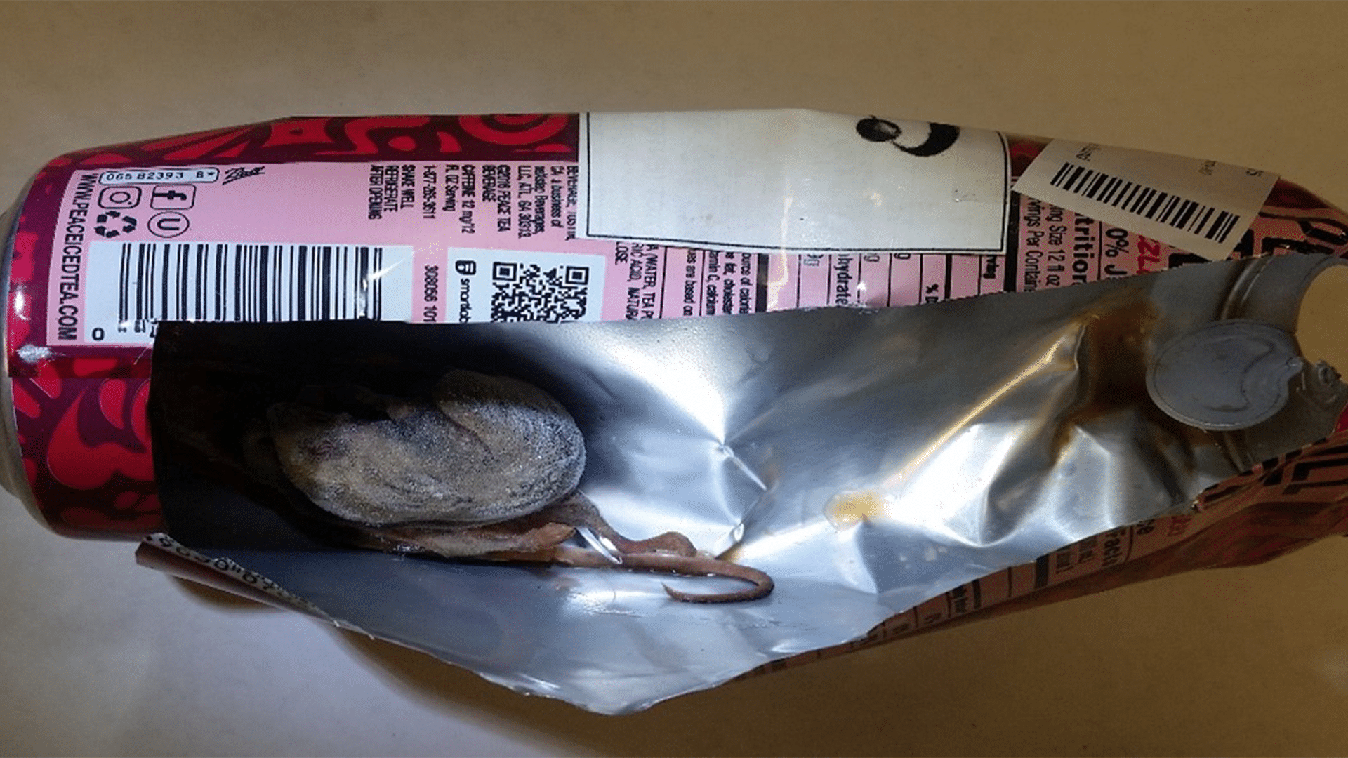 Rodent - Certified Laboratories Crushed soda can with torn foil wrapper, revealing a dead mouse inside.