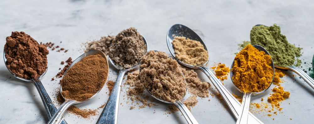 Variety of spices in metal spoons arranged in a row on a table.